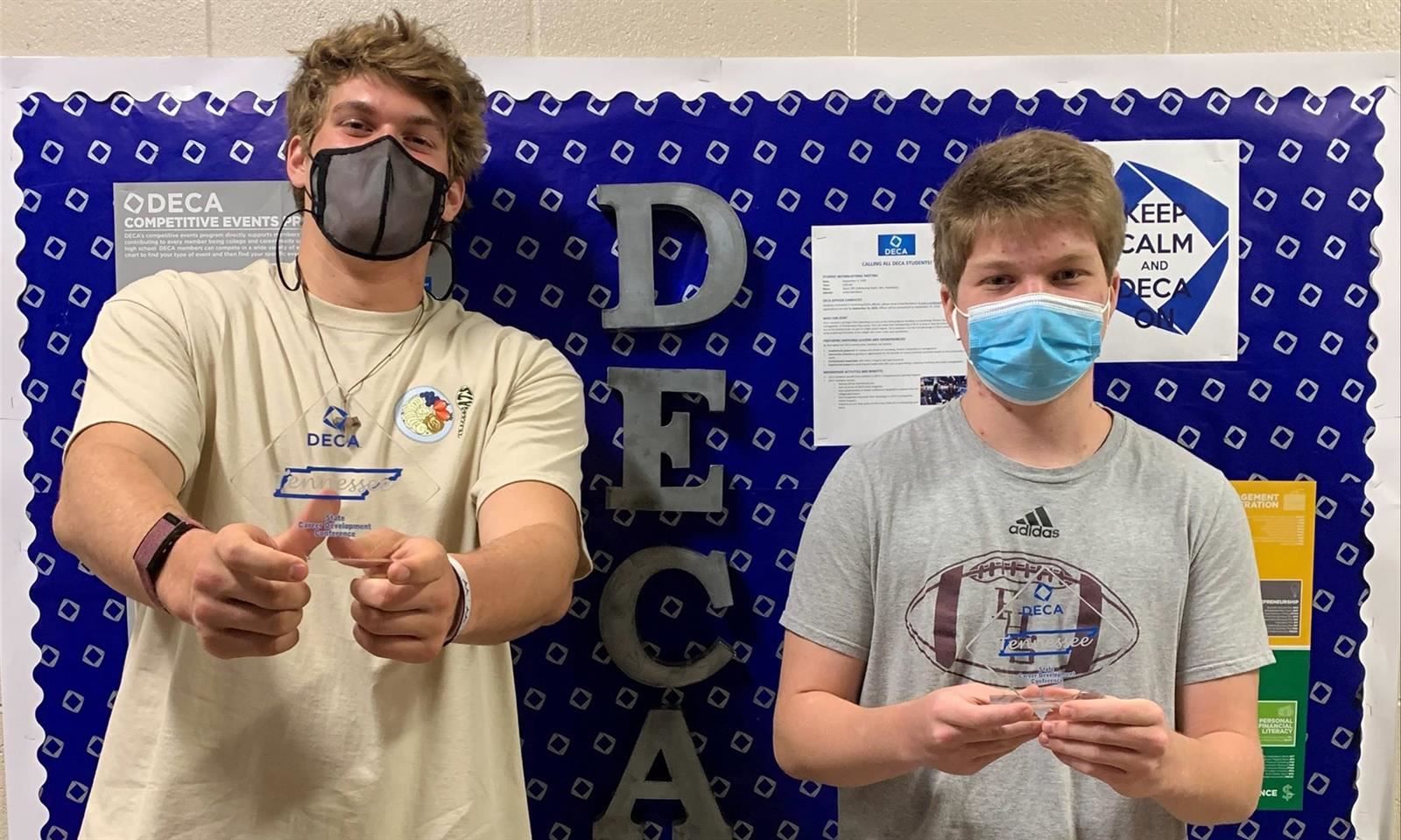 Two young men hold up DECA trophies 